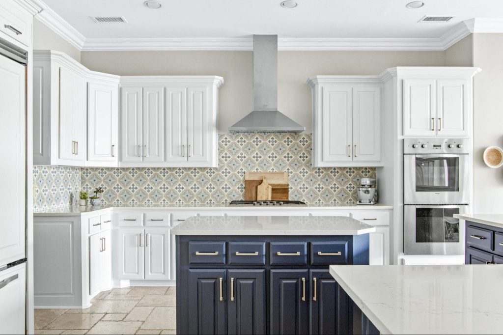 Two-tone kitchen with white upper cabinets and navy blue island, encaustic tile backsplash in warm tones, and brushed gold hardware — bold colorful kitchen design by Kitchen Design Concepts Dallas
